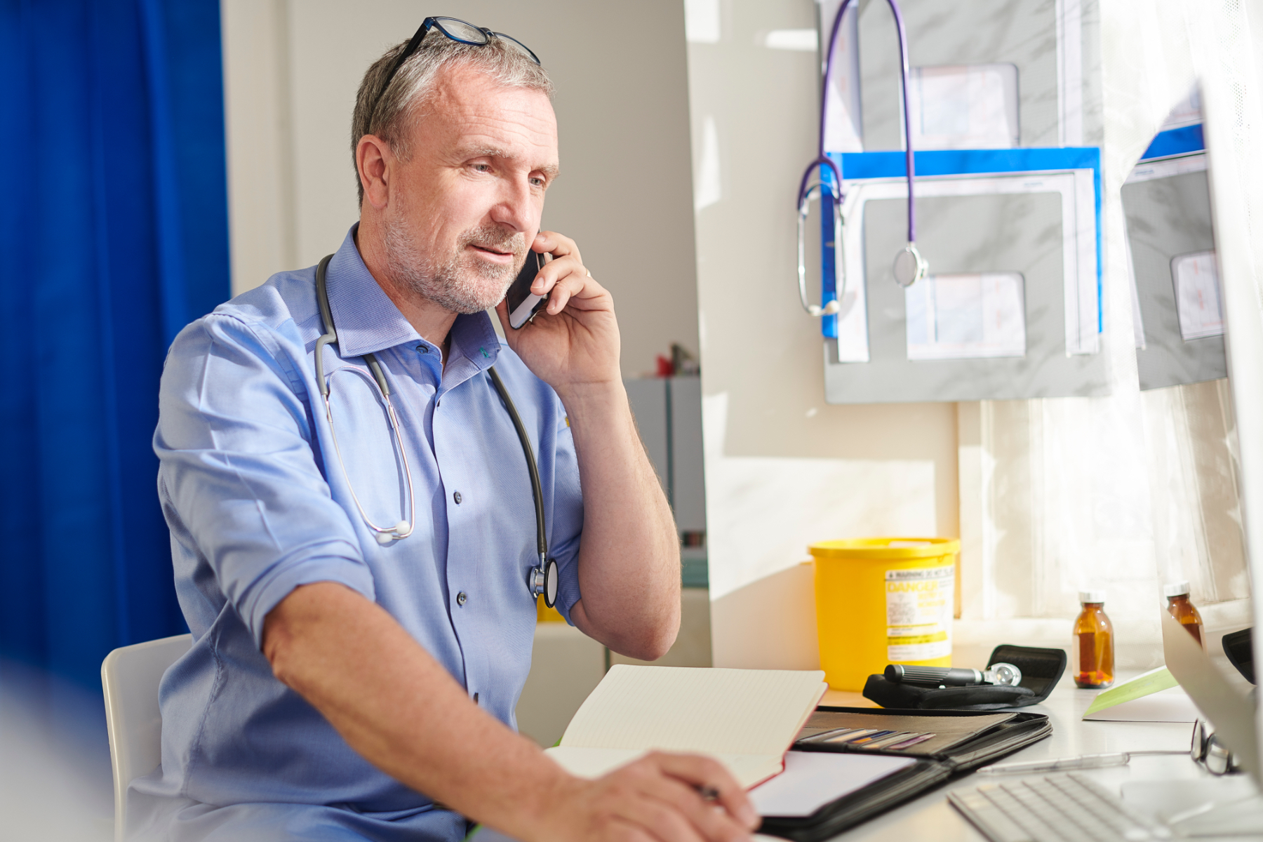 Image of a doctor sitting at his desk and making a call on a smartphone