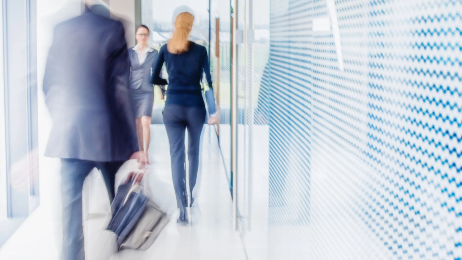 Motion blurred professionals walking through bright, modern hallway.