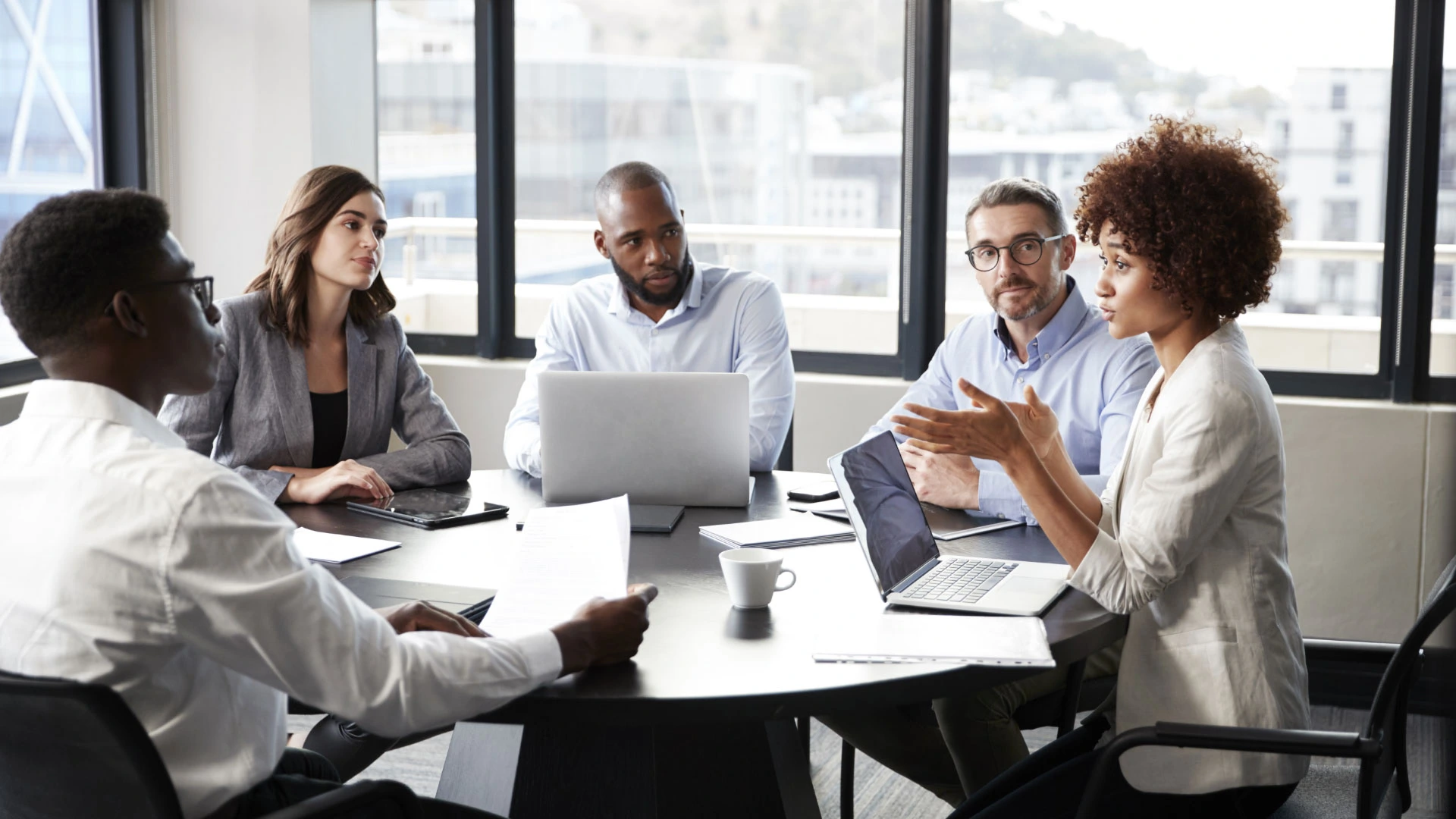 Five professionals engaged in a discussion around a table in a modern office.