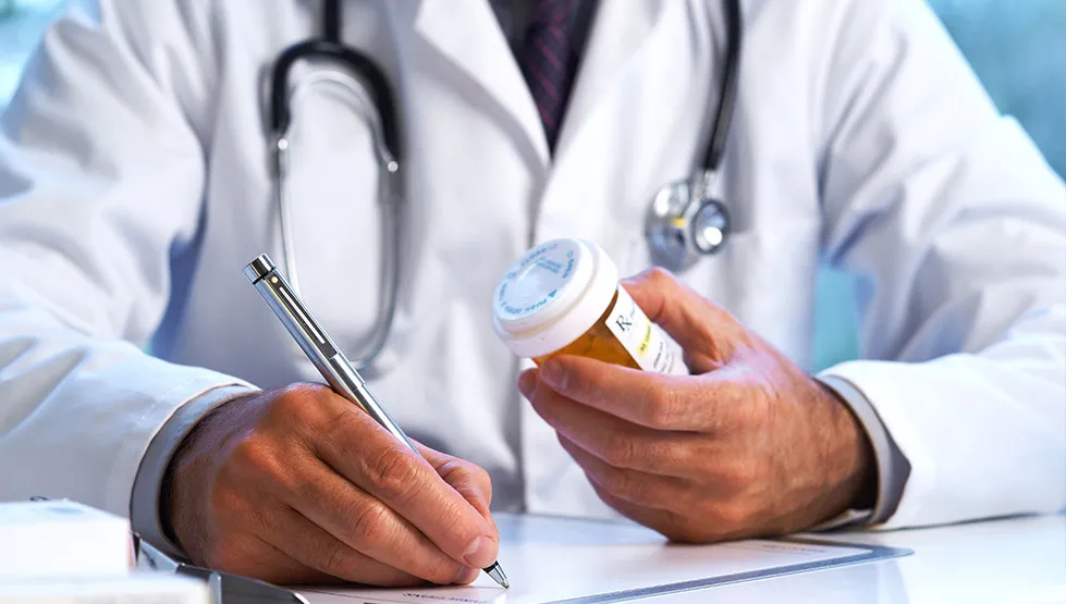 Doctor writing prescription while holding pill bottle